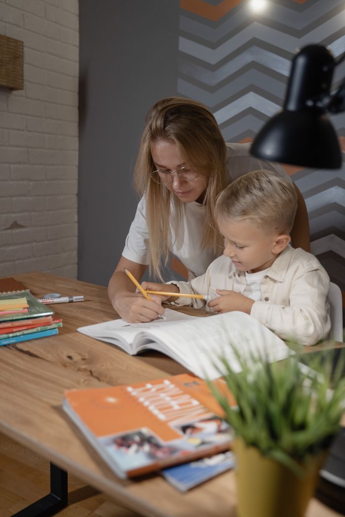 Mother guiding young child in homework indoors, promoting learning and education.